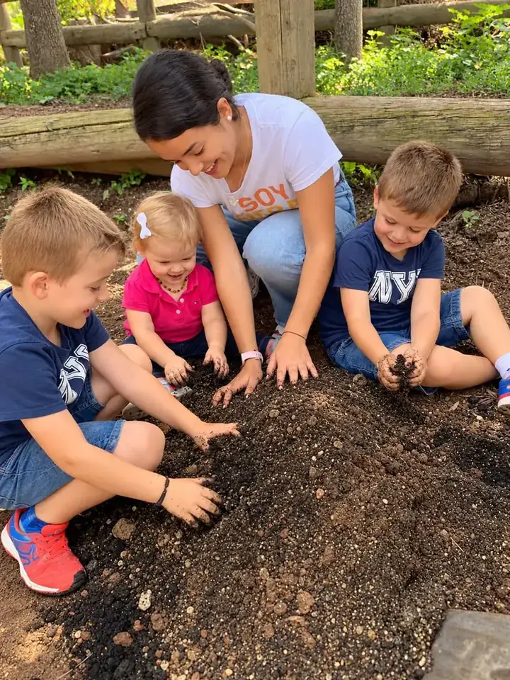 Cuatro niños y su niñera jugando con tierra en el jardín